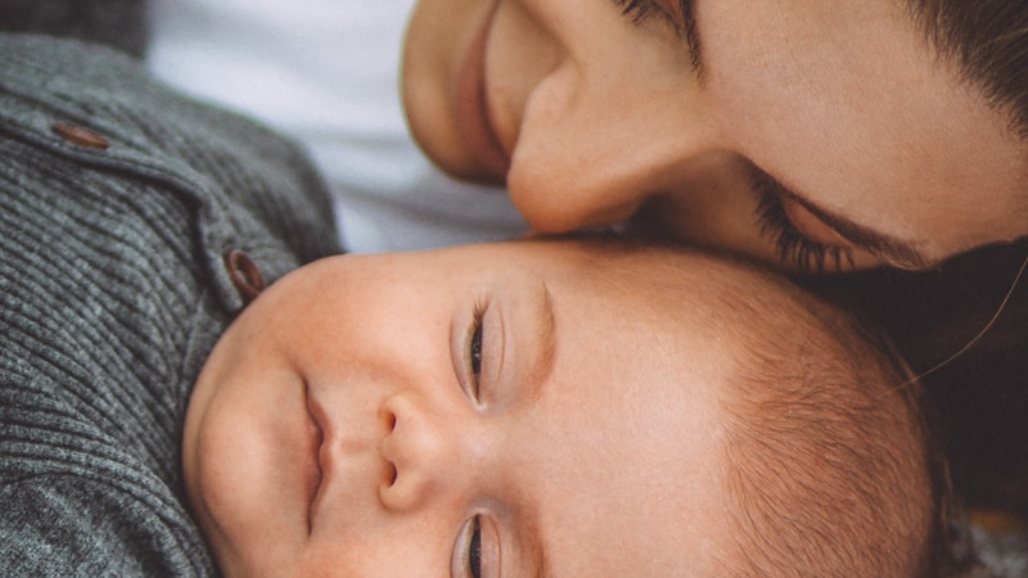 woman in gray shirt lying on bed beside baby