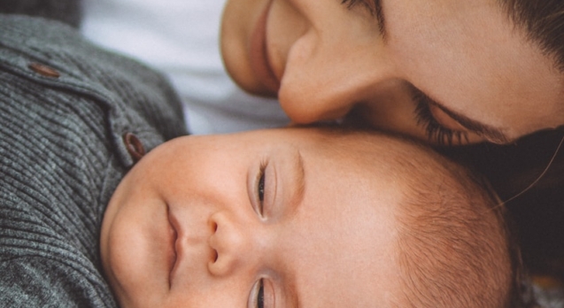 woman in gray shirt lying on bed beside baby