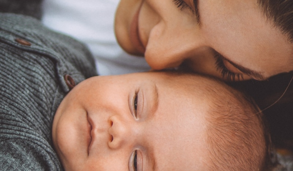 woman in gray shirt lying on bed beside baby