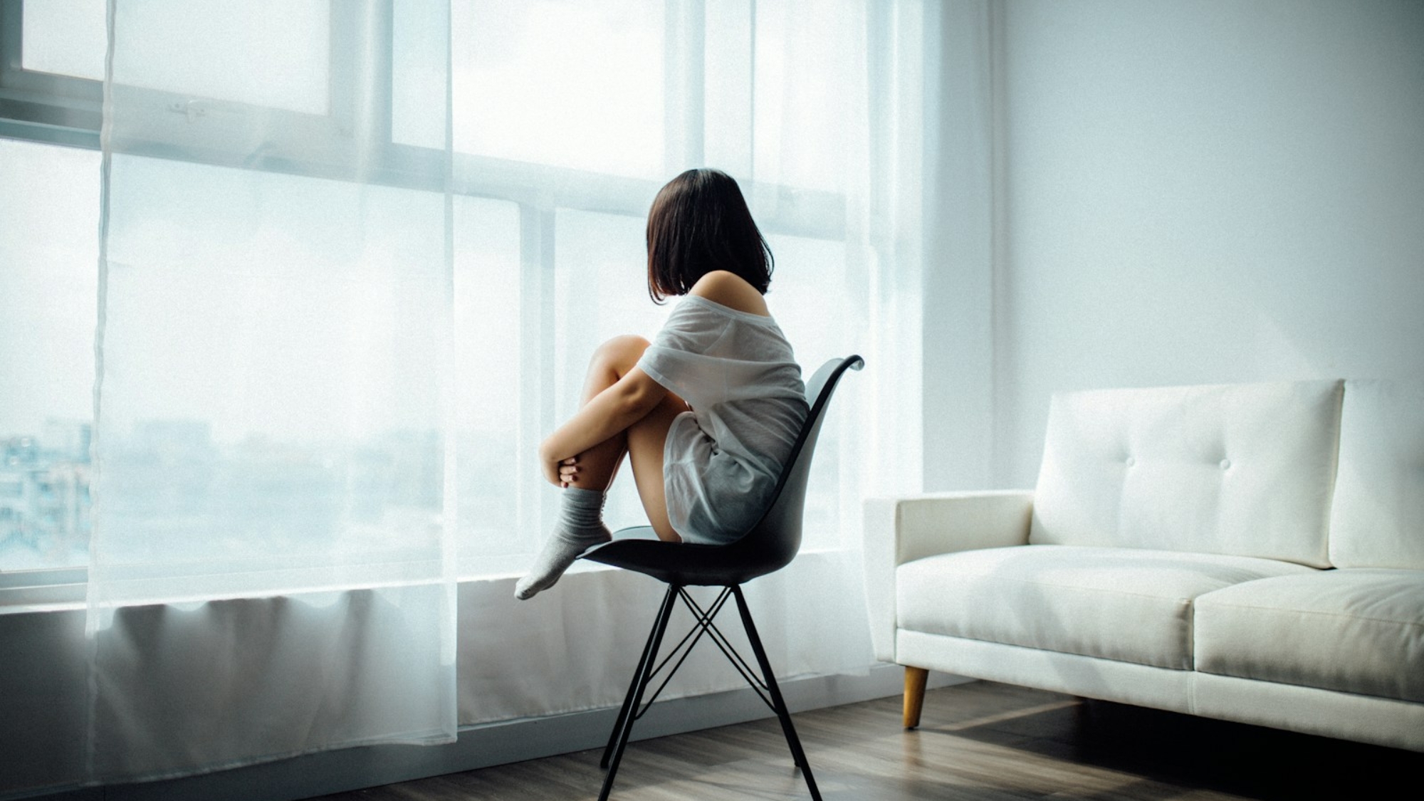 woman sitting on black chair in front of glass-panel window with white curtains